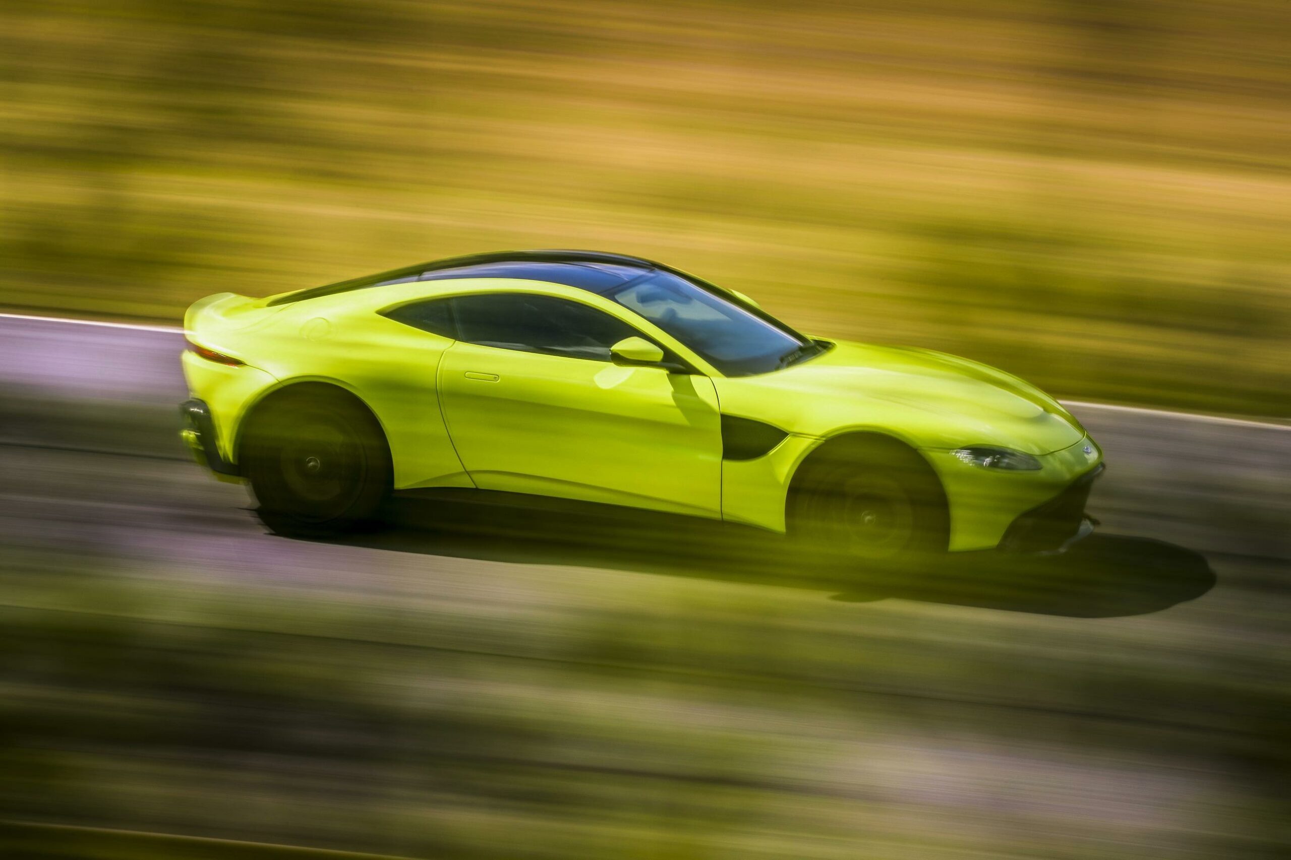 A side view of a neon yellow Aston Martin V8 Vantage driving down a road